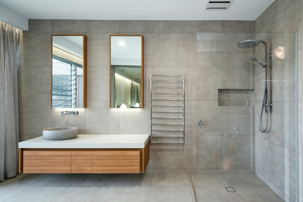 This is an example of a contemporary master bathroom in Adelaide with flat-panel cabinets, medium wood cabinets, a corner shower, beige tile, cement tile, beige walls, cement tiles, a vessel sink, beige floor, an open shower and beige benchtops.