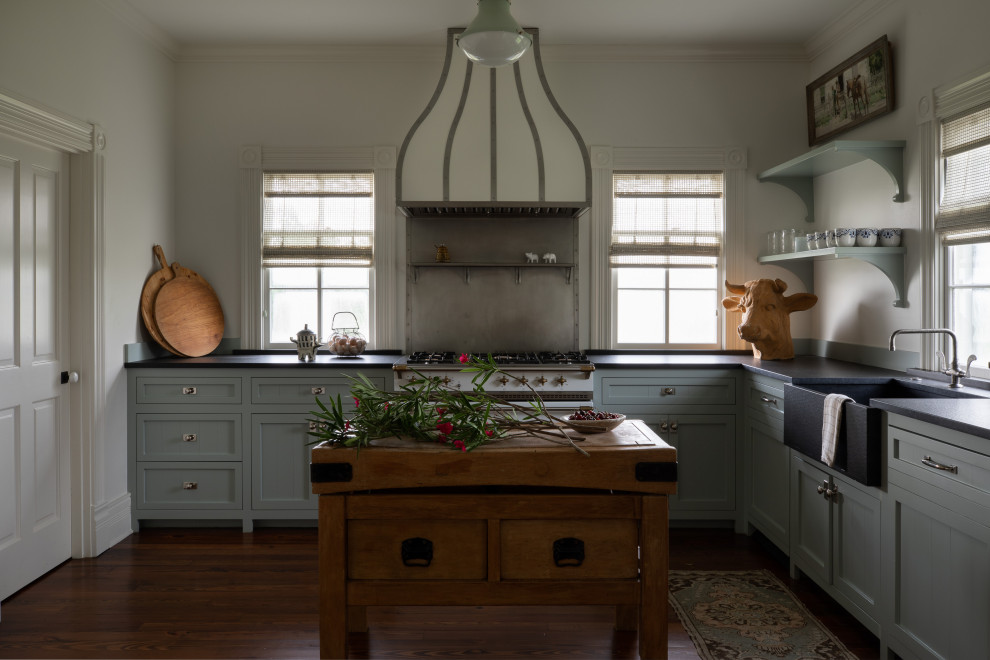 Inredning av ett klassiskt avskilt, mellanstort svart svart l-kök, med en rustik diskho, luckor med infälld panel, blå skåp, grått stänkskydd, vita vitvaror, mörkt trägolv, en köksö och brunt golv