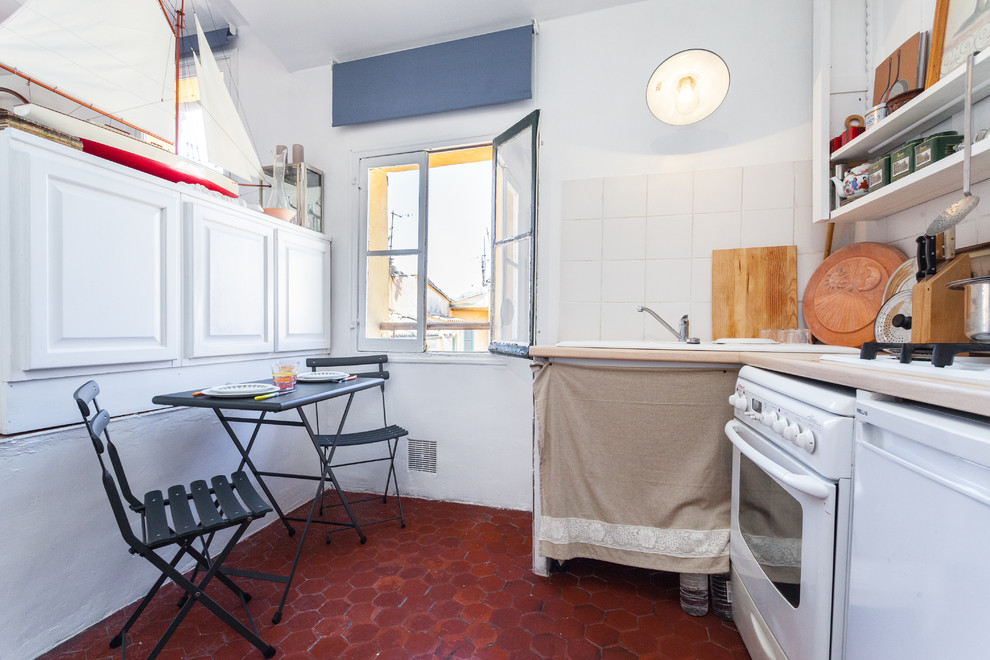 Photo of a small beach style l-shaped eat-in kitchen in Nice with a drop-in sink, open cabinets, white splashback, ceramic splashback, white appliances, terra-cotta floors and no island.