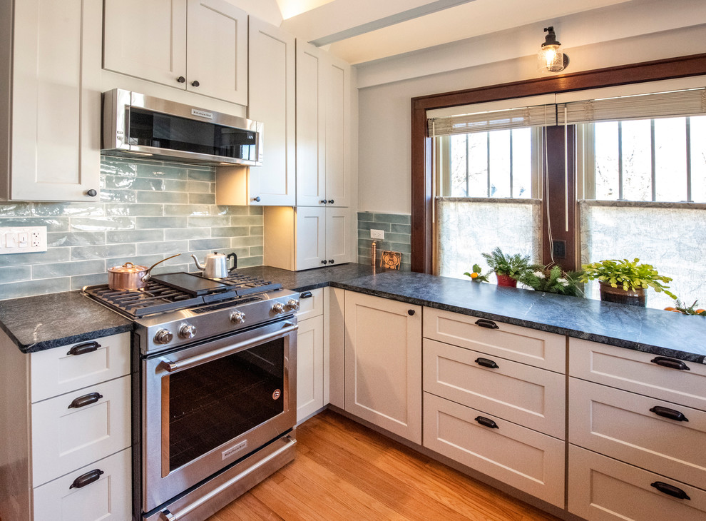 Photo of a small arts and crafts u-shaped eat-in kitchen in Chicago with a farmhouse sink, shaker cabinets, grey cabinets, granite benchtops, blue splashback, glass tile splashback, stainless steel appliances, medium hardwood floors, no island, brown floor and green benchtop.