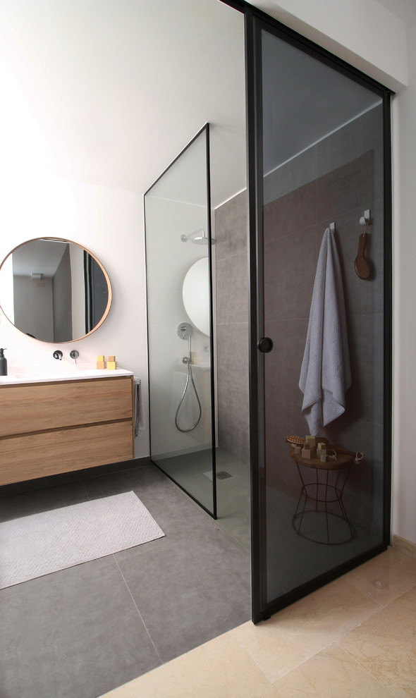 This is an example of a mid-sized modern master bathroom in Valencia with flat-panel cabinets, medium wood cabinets, an open shower, a wall-mount toilet, gray tile, white walls, an integrated sink, grey floor and white benchtops.