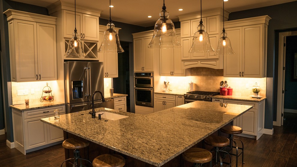 Large transitional u-shaped dark wood floor and brown floor eat-in kitchen photo in Austin with an undermount sink, raised-panel cabinets, white cabinets, granite countertops, beige backsplash, travertine backsplash, stainless steel appliances, an island and multicolored countertops