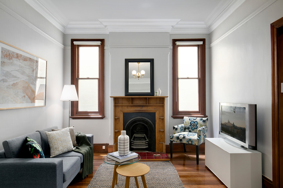 Transitional enclosed living room in Sydney with medium hardwood floors, a standard fireplace, a wood fireplace surround, a freestanding tv, brown floor and grey walls.
