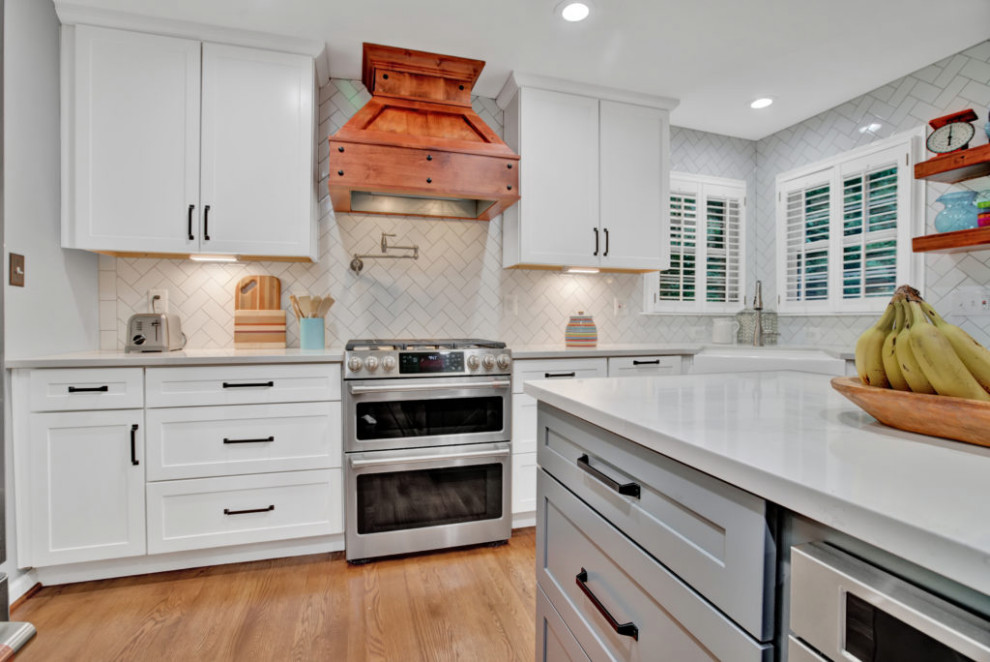 Photo of a large modern kitchen/diner in DC Metro with a submerged sink, shaker cabinets, white cabinets, engineered stone countertops, white splashback, cement tile splashback, stainless steel appliances, medium hardwood flooring, an island, brown floors and white worktops.
