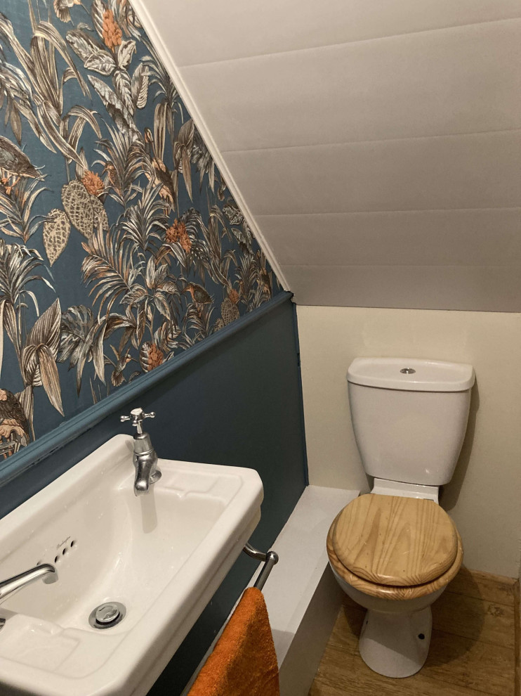 Design ideas for a small victorian cloakroom in Other with a one-piece toilet, blue walls, laminate floors, a wall-mounted sink, brown floors, a feature wall and wallpapered walls.