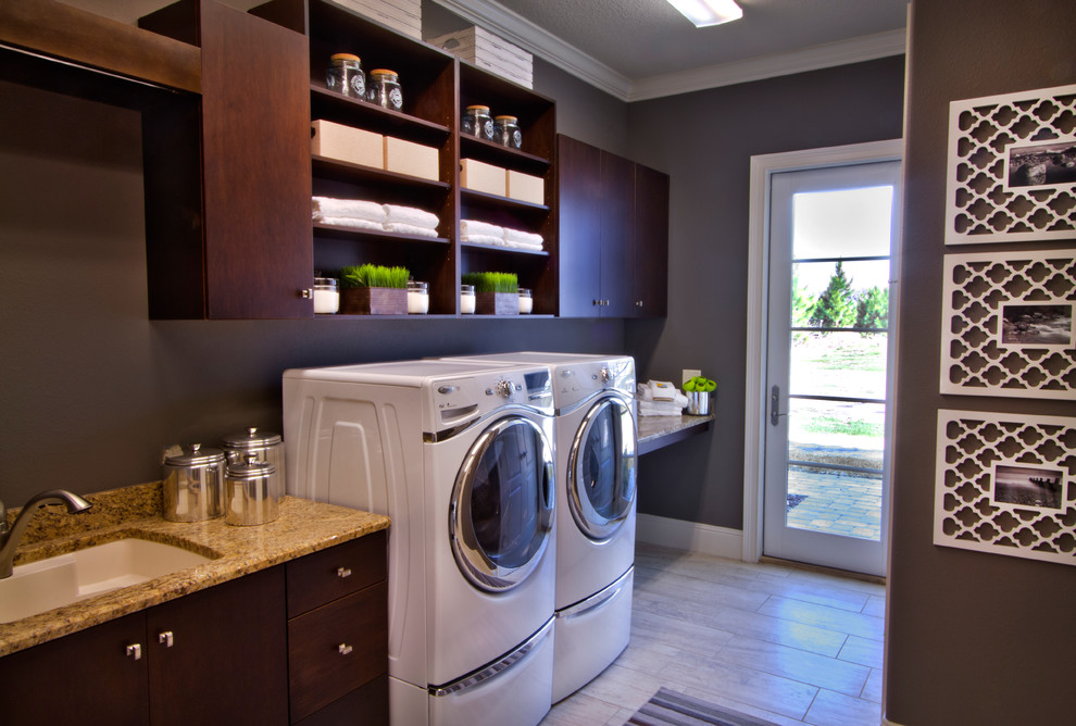 Design ideas for a mid-sized mediterranean l-shaped dedicated laundry room in Orlando with flat-panel cabinets, dark wood cabinets, granite benchtops, grey walls, light hardwood floors, a side-by-side washer and dryer and an undermount sink.
