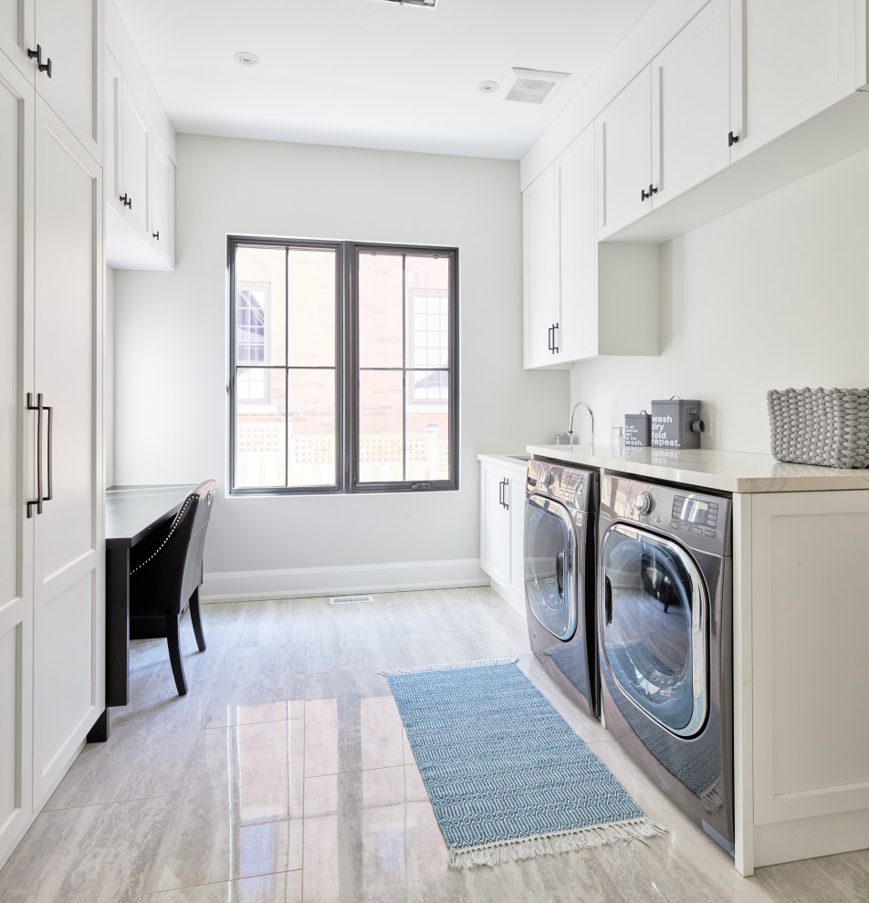 Photo of a mid-sized transitional galley dedicated laundry room in Toronto with an undermount sink, recessed-panel cabinets, white cabinets, onyx benchtops, white walls, porcelain floors, a side-by-side washer and dryer, grey floor and white benchtop.