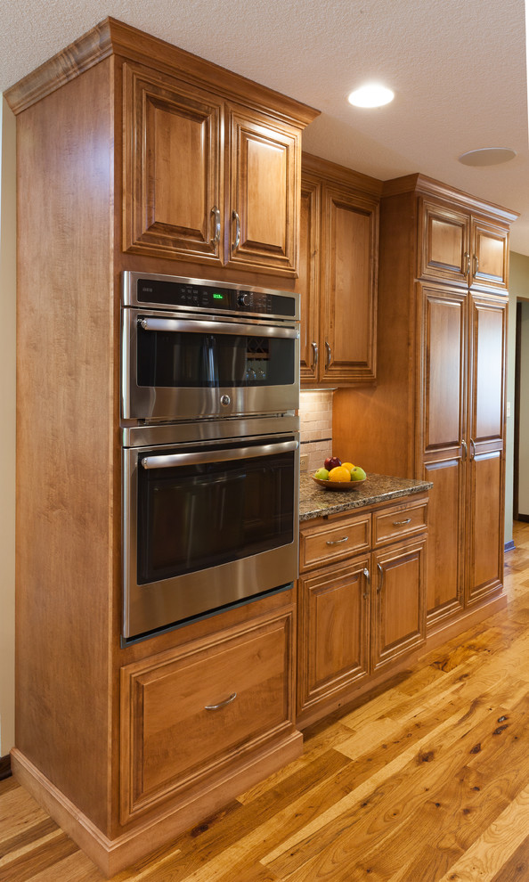 Photo of a mid-sized traditional l-shaped eat-in kitchen in Minneapolis with an undermount sink, recessed-panel cabinets, dark wood cabinets, granite benchtops, white splashback, porcelain splashback, stainless steel appliances, light hardwood floors, with island and beige floor.