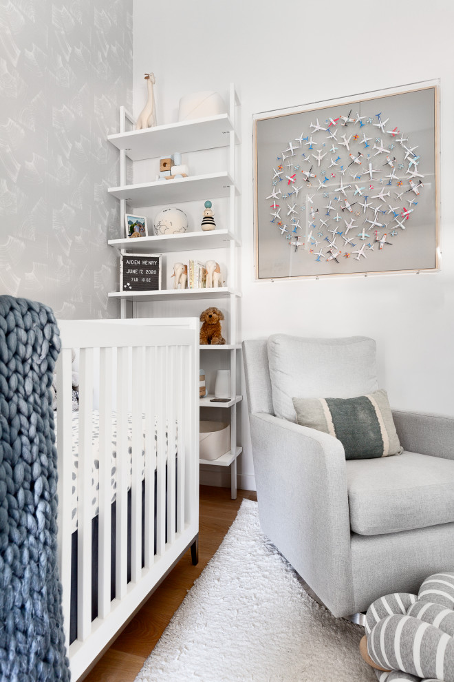 Design ideas for a small contemporary nursery for boys in New York with white walls, light hardwood floors and wallpaper.
