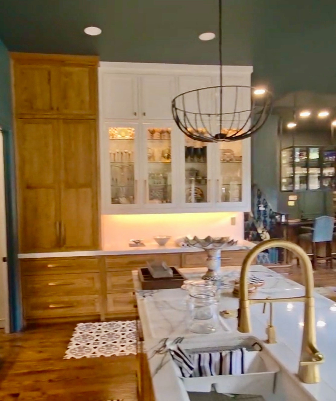Dual-tone cabinetry design featuring natural wood lower cabinets paired with off-white, floor-to-ceiling upper cabinets and glass-front display sections with glass shelving.