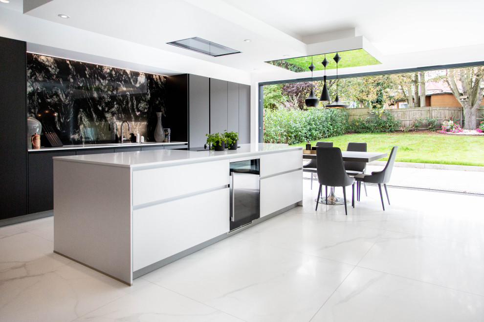 This is an example of an expansive contemporary galley eat-in kitchen in London with with island, flat-panel cabinets, black cabinets, black splashback, panelled appliances, white floor and white benchtop.