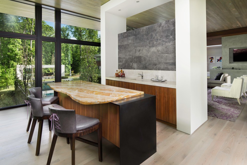 Inspiration for a large contemporary single-wall seated home bar in Atlanta with an integrated sink, flat-panel cabinets, medium wood cabinets, onyx benchtops, grey splashback, stone slab splashback, light hardwood floors, beige floor and multi-coloured benchtop.