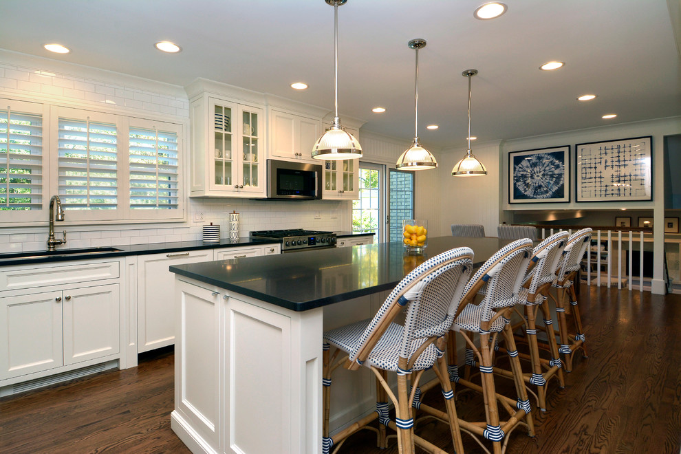 Eat-in kitchen - large transitional l-shaped medium tone wood floor eat-in kitchen idea in Chicago with a farmhouse sink, shaker cabinets, white cabinets, granite countertops, white backsplash, subway tile backsplash, stainless steel appliances and an island
