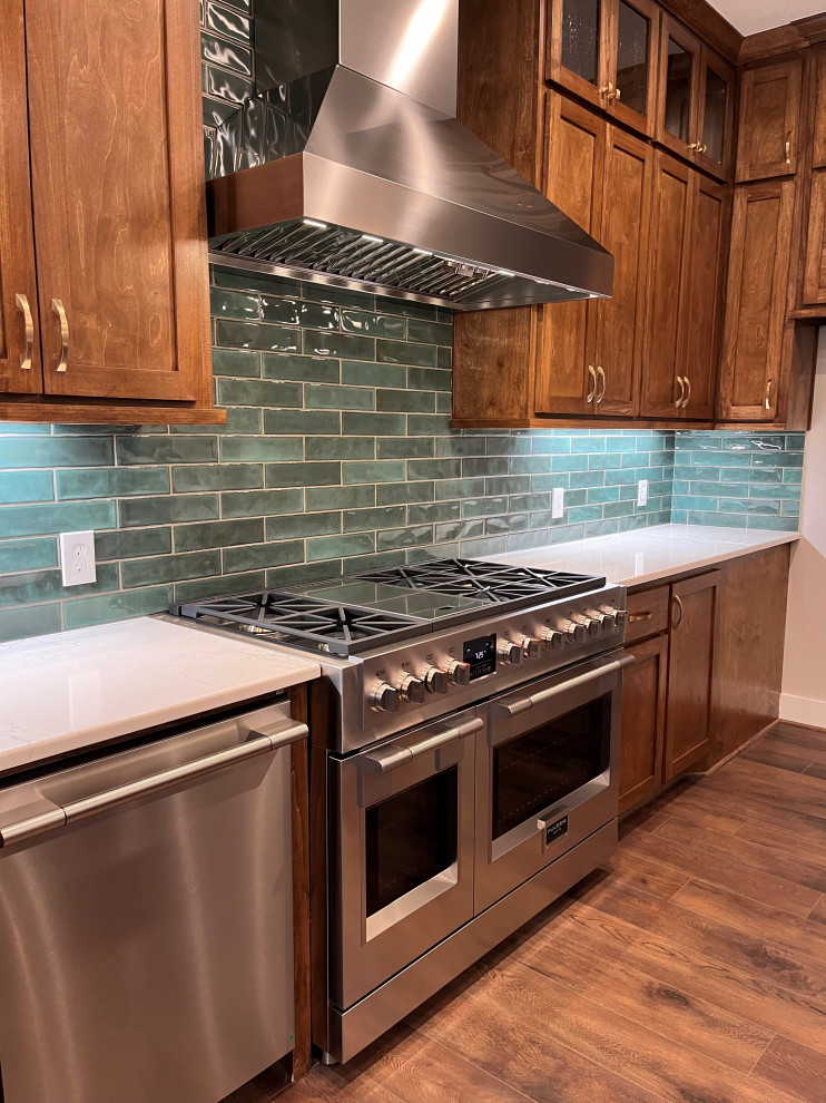 Example of a transitional vinyl floor and brown floor kitchen design in Houston with shaker cabinets, brown cabinets, quartz countertops, green backsplash, porcelain backsplash, stainless steel appliances and white countertops