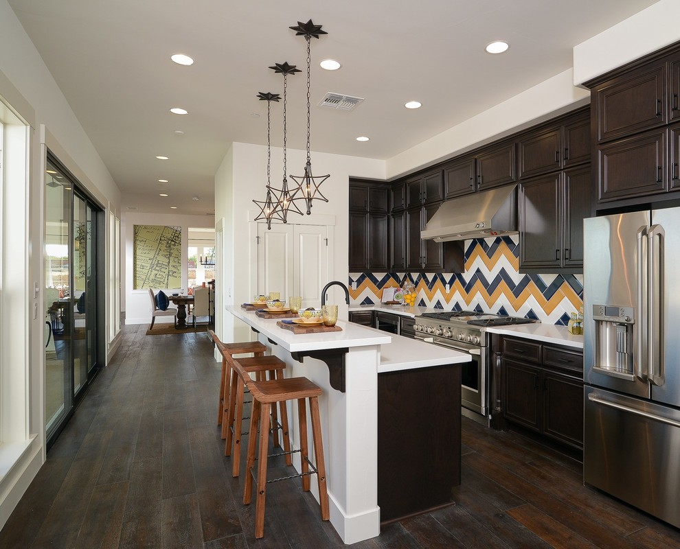 This is an example of a large transitional l-shaped eat-in kitchen in Sacramento with raised-panel cabinets, dark wood cabinets, quartz benchtops, multi-coloured splashback, subway tile splashback, stainless steel appliances, dark hardwood floors and with island.