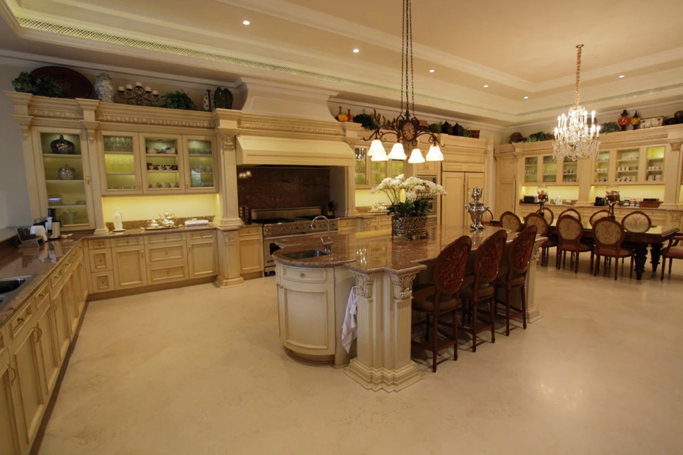 Photo of an expansive traditional u-shaped eat-in kitchen in Los Angeles with an undermount sink, glass-front cabinets, beige cabinets, stainless steel appliances, with island and beige floor.