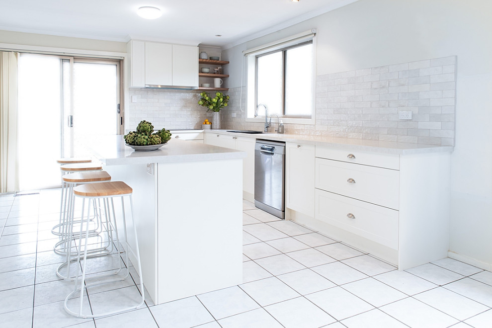 Photo of a large modern u-shaped kitchen/diner in Melbourne with a built-in sink, shaker cabinets, white cabinets, engineered stone countertops, white splashback, metro tiled splashback, stainless steel appliances, porcelain flooring, an island, white floors and grey worktops.