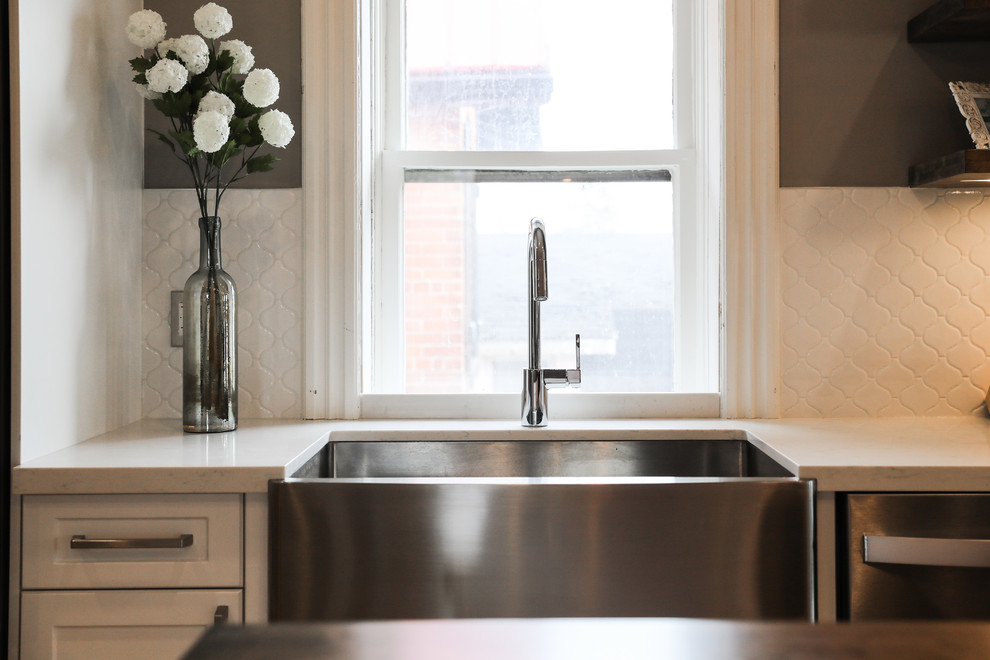 Eat-in kitchen - mid-sized transitional single-wall medium tone wood floor and brown floor eat-in kitchen idea with a farmhouse sink, shaker cabinets, white cabinets, white backsplash, stainless steel appliances, an island and white countertops