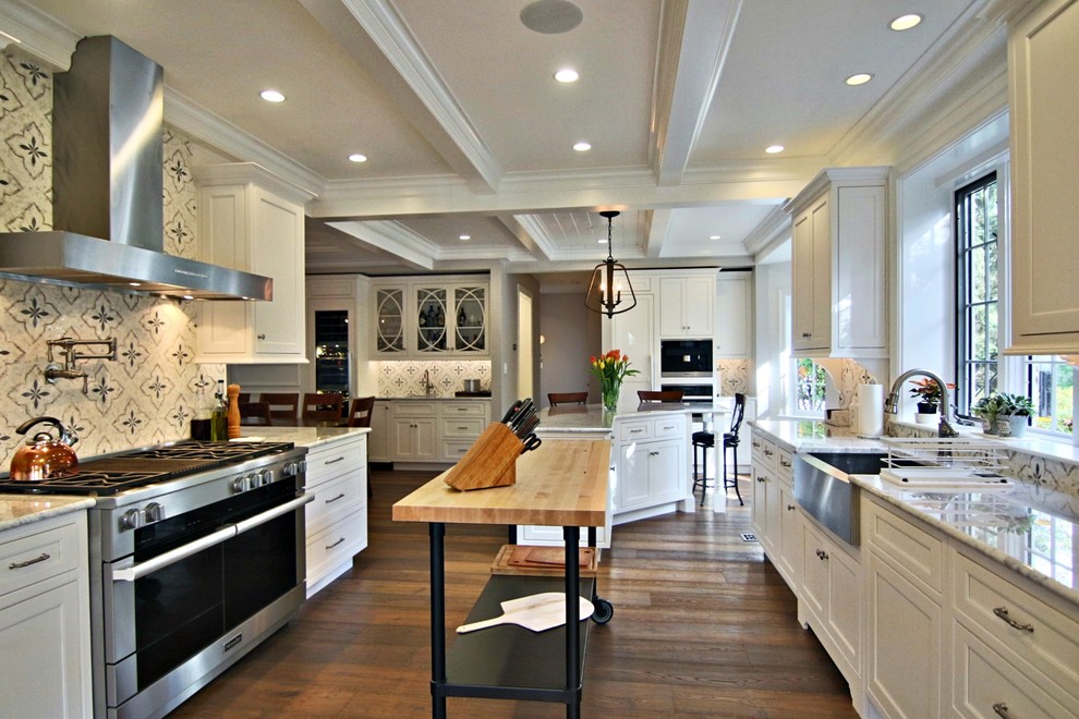 Example of a large transitional l-shaped laminate floor and brown floor open concept kitchen design in Boston with a farmhouse sink, recessed-panel cabinets, white cabinets, marble countertops, white backsplash, marble backsplash, paneled appliances and an island