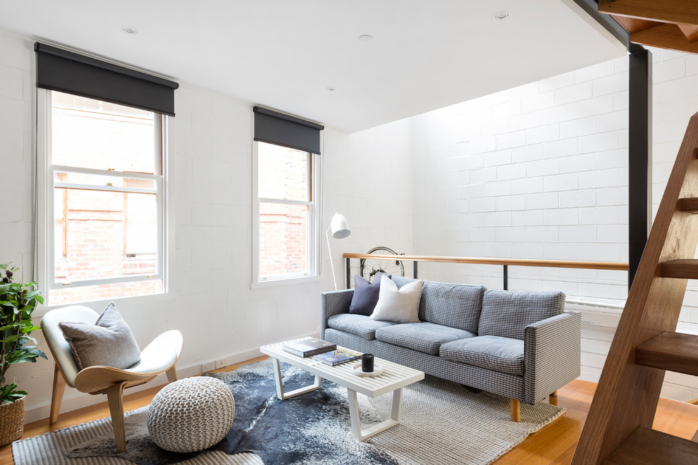 Photo of a scandinavian formal loft-style living room in Melbourne with white walls, medium hardwood floors and brown floor.