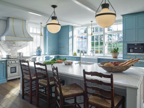 RTA cabinets in a light blue kitchen with marble island, brass hardware, farmhouse sink, and globe pendants.