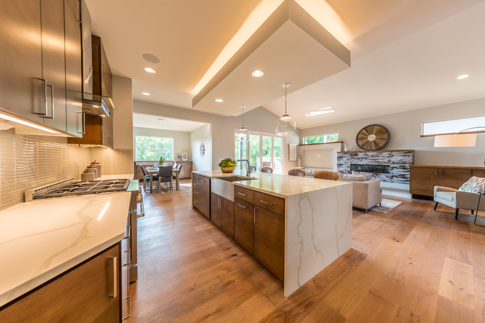 Large contemporary l-shaped eat-in kitchen in Portland with a farmhouse sink, flat-panel cabinets, brown cabinets, quartz benchtops, grey splashback, glass tile splashback, stainless steel appliances, light hardwood floors, with island and brown floor.