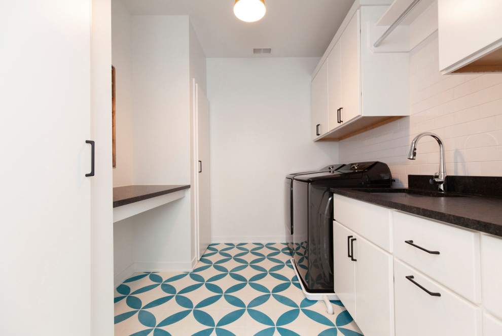 This is an example of a large modern galley dedicated laundry room in Chicago with an undermount sink, flat-panel cabinets, white cabinets, quartz benchtops, white splashback, subway tile splashback, white walls, porcelain floors, a side-by-side washer and dryer, turquoise floor and black benchtop.