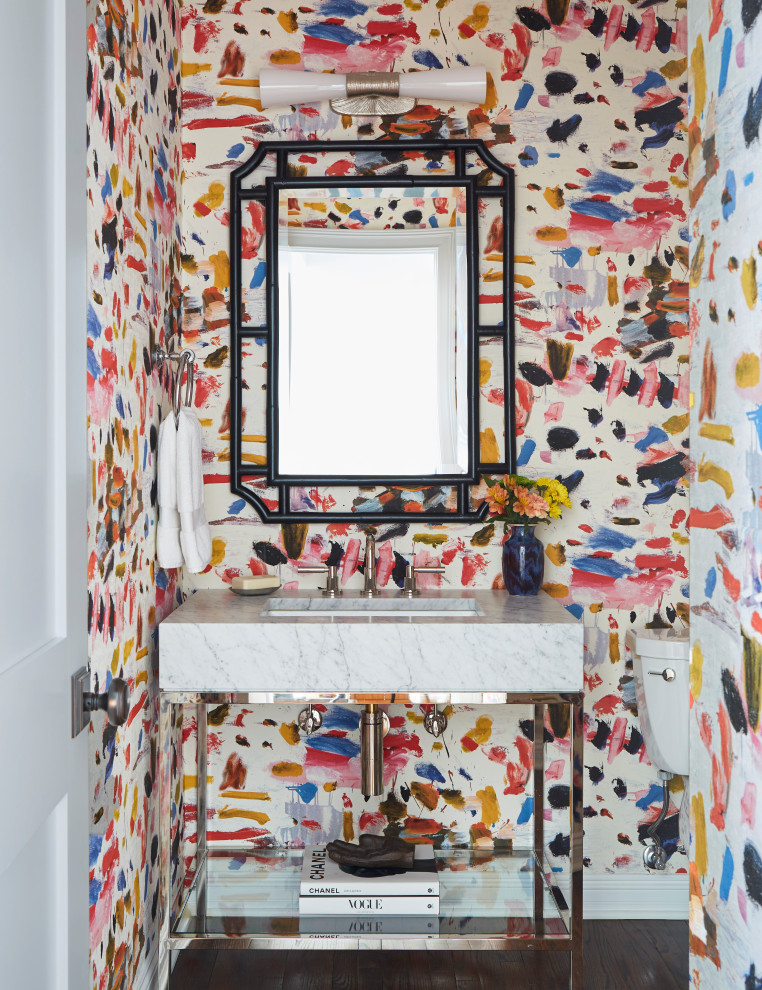 Example of a mid-sized transitional medium tone wood floor, brown floor and wallpaper powder room design in Chicago with a two-piece toilet, multicolored walls, an undermount sink, marble countertops, white countertops and a freestanding vanity