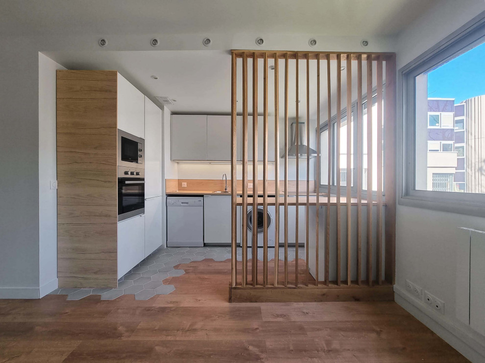 Skandinavisk inredning av ett mellanstort beige beige kök, med en undermonterad diskho, luckor med profilerade fronter, vita skåp, träbänkskiva, beige stänkskydd, stänkskydd i trä, vita vitvaror, cementgolv, en köksö och grått golv