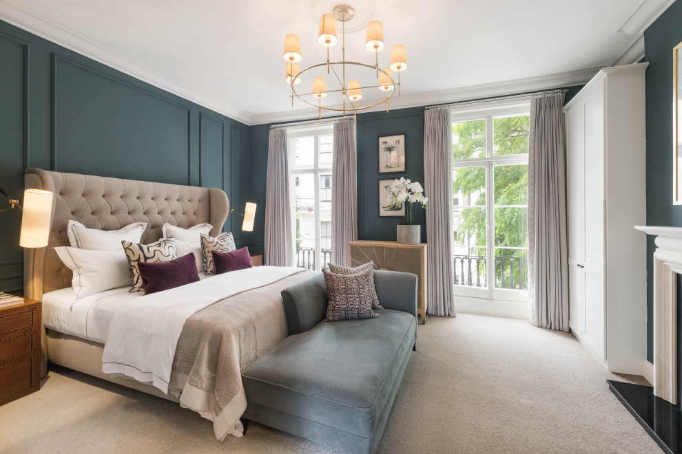ロンドンにある中くらいなトランジショナルスタイルのおしゃれな主寝室 (青い壁、カーペット敷き、標準型暖炉、石材の暖炉まわり、ベージュの床、パネル壁) のインテリア