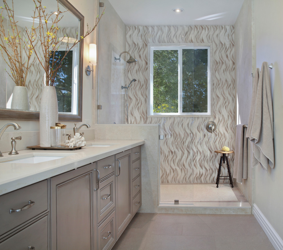 Inspiration for a mid-sized transitional master bathroom in Orange County with recessed-panel cabinets, grey cabinets, engineered quartz benchtops, a freestanding tub, an open shower, stone tile, beige walls, ceramic floors, a drop-in sink, beige floor and a hinged shower door.