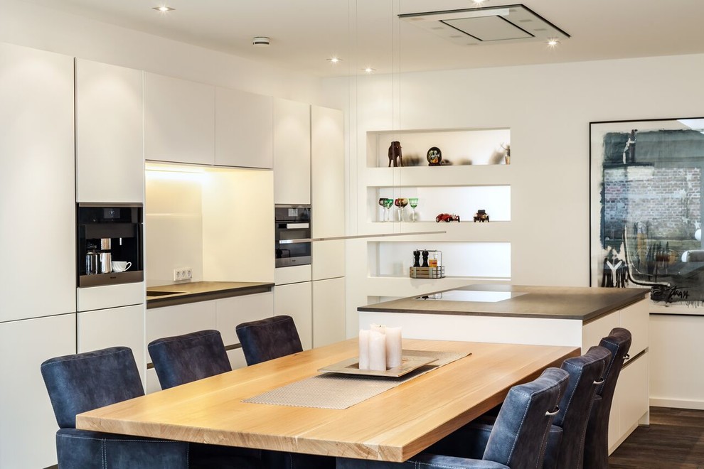 Large contemporary single-wall open plan kitchen in Dortmund with an undermount sink, flat-panel cabinets, white cabinets, solid surface benchtops, white splashback, glass sheet splashback, stainless steel appliances, painted wood floors and with island.