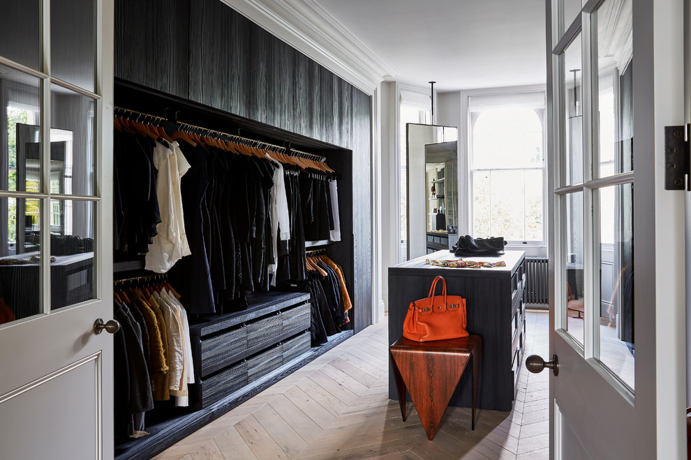 Photo of a contemporary gender-neutral dressing room in London with open cabinets, black cabinets and light hardwood floors.