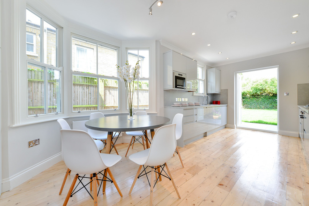 Photo of a medium sized contemporary galley kitchen/diner in London with a double-bowl sink, flat-panel cabinets, grey cabinets, composite countertops, grey splashback, window splashback, stainless steel appliances, light hardwood flooring, no island, grey worktops and beige floors.
