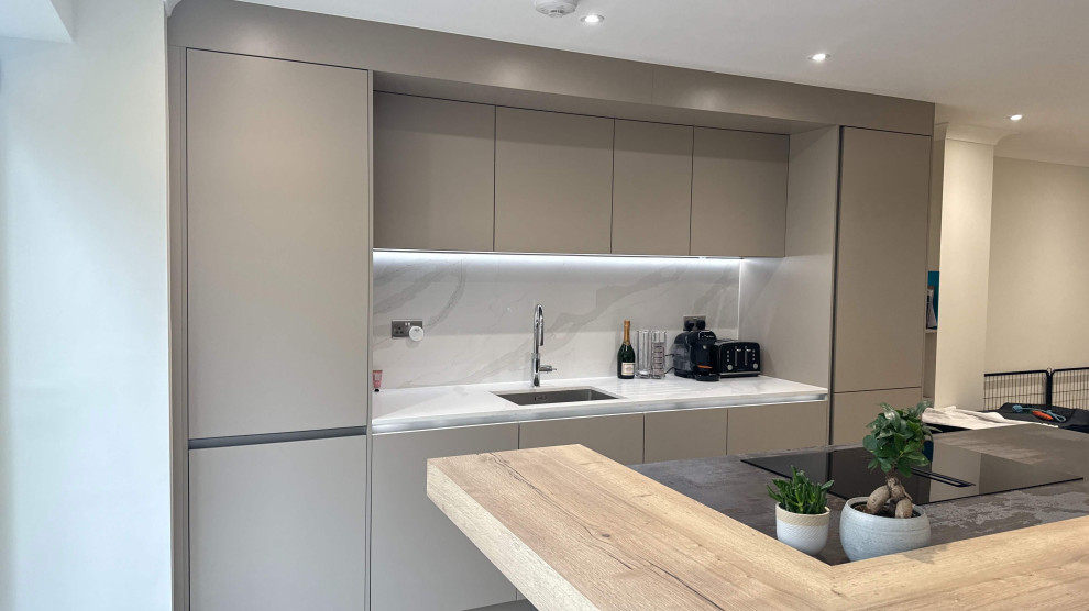 Inspiration for a mid-sized contemporary single-wall open plan kitchen in London with a single-bowl sink, flat-panel cabinets, grey cabinets, quartzite benchtops, grey splashback, panelled appliances, with island, grey floor and grey benchtop.