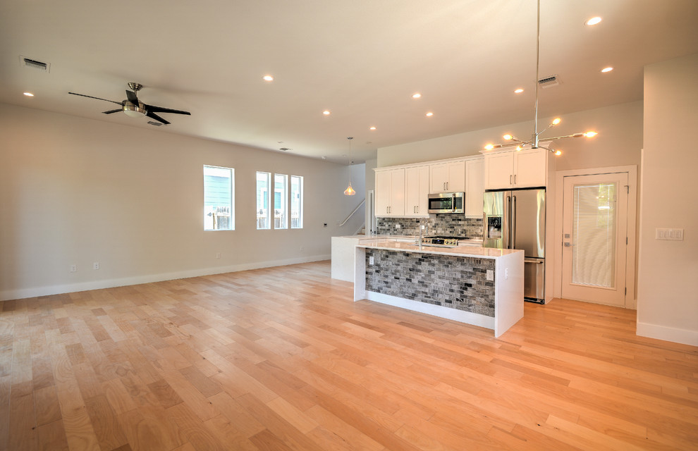 Example of a mid-sized transitional single-wall medium tone wood floor and brown floor open concept kitchen design in Austin with a double-bowl sink, shaker cabinets, white cabinets, marble countertops, gray backsplash, stone tile backsplash, stainless steel appliances, an island and white countertops