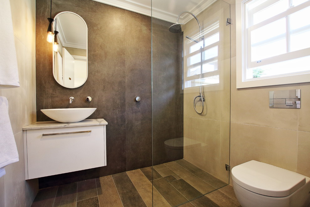 This is an example of a mid-sized contemporary bathroom in Sydney with flat-panel cabinets, white cabinets, a corner shower, a wall-mount toilet, brown tile, porcelain tile, brown walls, porcelain floors, a vessel sink, engineered quartz benchtops, brown floor, an open shower and white benchtops.