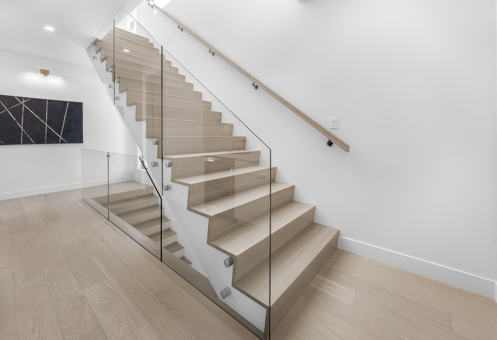 Réalisation d'un grand escalier minimaliste avec des marches en bois, des contremarches en moquette et un garde-corps en verre.