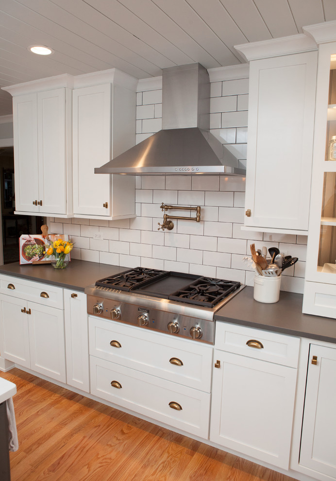 Inspiration for a mid-sized transitional u-shaped light wood floor eat-in kitchen remodel in Chicago with a farmhouse sink, recessed-panel cabinets, white cabinets, quartz countertops, multicolored backsplash, subway tile backsplash, stainless steel appliances and an island