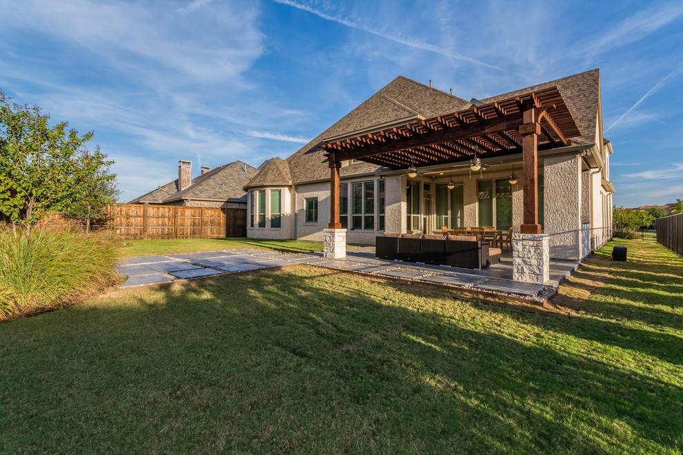 This is an example of a large transitional backyard patio in Dallas with an outdoor kitchen, stamped concrete and a pergola.