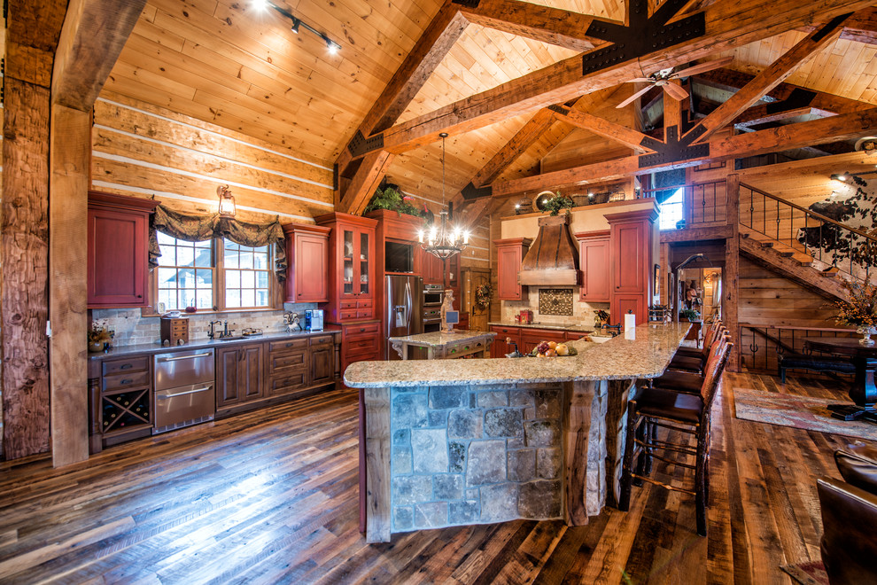 Huge mountain style l-shaped dark wood floor open concept kitchen photo with an undermount sink, beaded inset cabinets, red cabinets, granite countertops, beige backsplash, stone tile backsplash, stainless steel appliances and two islands