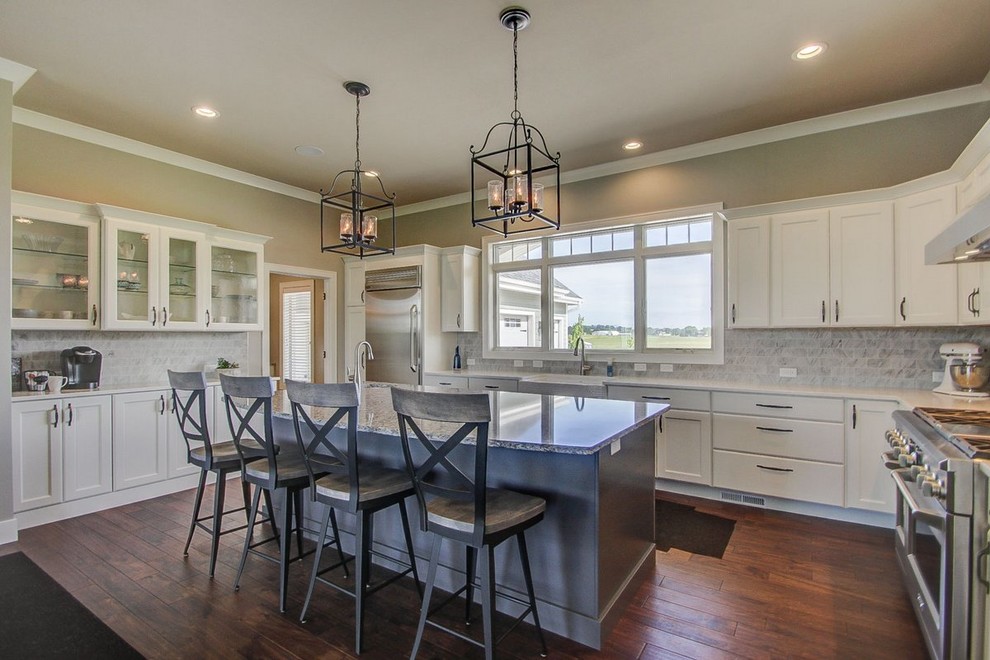 Inspiration for a large transitional l-shaped medium tone wood floor kitchen remodel with a farmhouse sink, recessed-panel cabinets, white cabinets, stone tile backsplash, stainless steel appliances and an island