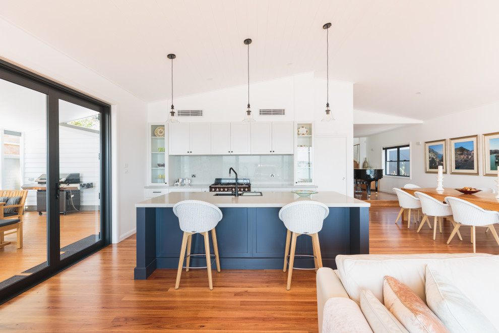 Photo of a large beach style open plan kitchen in Newcastle - Maitland with shaker cabinets, white cabinets, quartz benchtops, grey splashback, with island, white benchtop, an undermount sink, medium hardwood floors and vaulted.