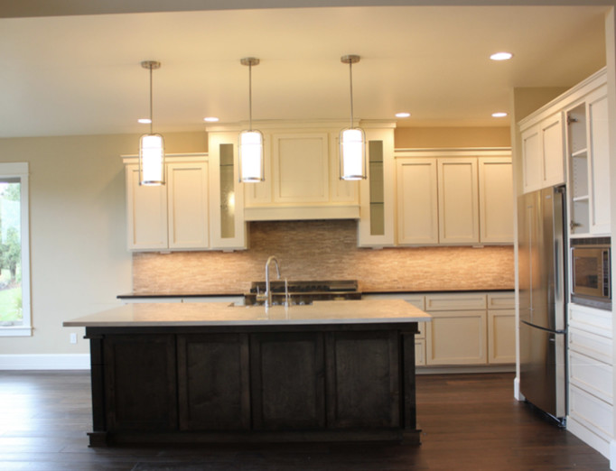 Example of a large transitional l-shaped dark wood floor and brown floor enclosed kitchen design with a farmhouse sink, shaker cabinets, white cabinets, quartz countertops, beige backsplash, stone tile backsplash, stainless steel appliances and an island