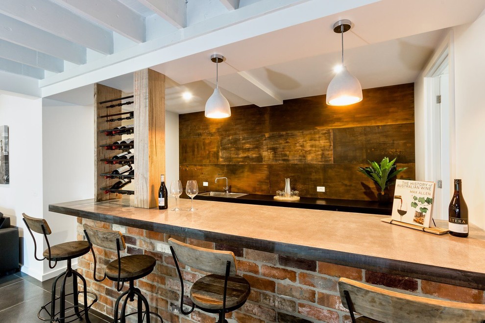 Large galley seated home bar in Other with a drop-in sink, black cabinets, concrete benchtops, brown splashback, porcelain floors, grey floor and grey benchtop.