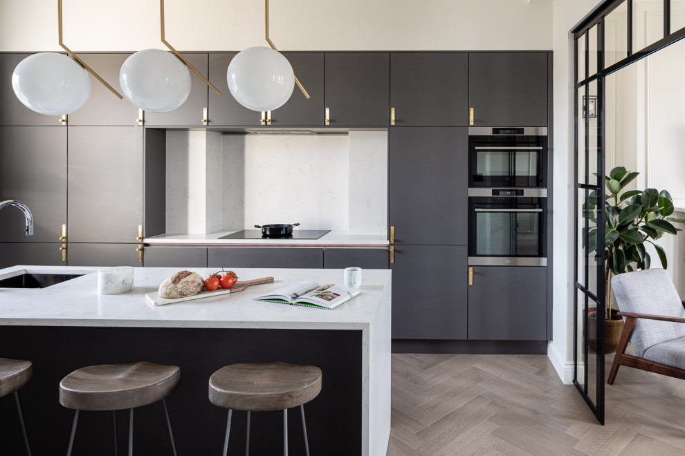 Inspiration for a large contemporary galley separate kitchen in London with an undermount sink, flat-panel cabinets, grey cabinets, white splashback, panelled appliances, with island, grey floor and white benchtop.