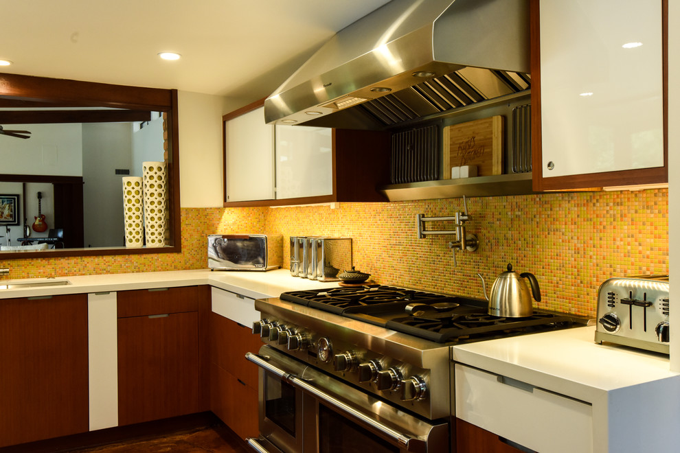 Photo of a midcentury u-shaped eat-in kitchen in Houston with an undermount sink, flat-panel cabinets, medium wood cabinets, solid surface benchtops, orange splashback, mosaic tile splashback, stainless steel appliances and with island.