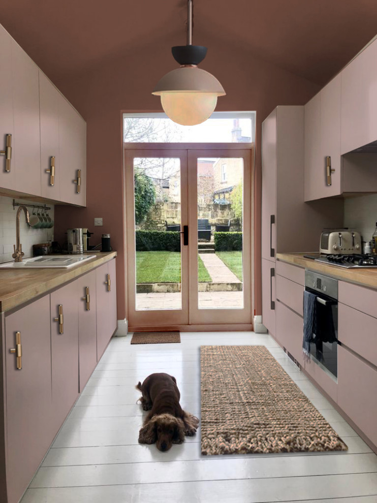 Design ideas for a mid-sized contemporary galley separate kitchen in London with a drop-in sink, flat-panel cabinets, pink cabinets, wood benchtops, white splashback, ceramic splashback, stainless steel appliances, painted wood floors, no island, white floor and beige benchtop.