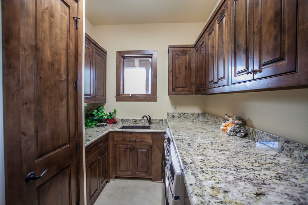 Inspiration for a small country galley dedicated laundry room in Austin with an undermount sink, raised-panel cabinets, dark wood cabinets, granite benchtops, beige walls, a side-by-side washer and dryer and beige floor.
