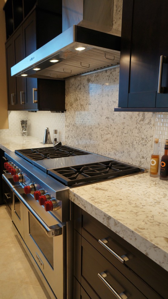 Example of a transitional l-shaped porcelain tile and beige floor kitchen design in Phoenix with an undermount sink, recessed-panel cabinets, dark wood cabinets, quartz countertops, white backsplash, ceramic backsplash, stainless steel appliances and an island